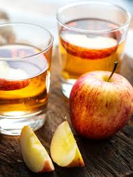 Two glasses of apple cider next to several slices of fresh apples