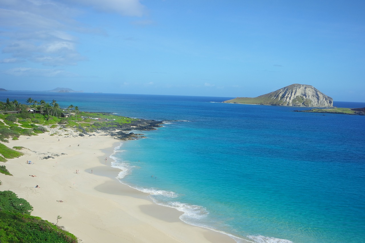 A beautiful beach in Hawaii with a clear ocean and a large island in the distance