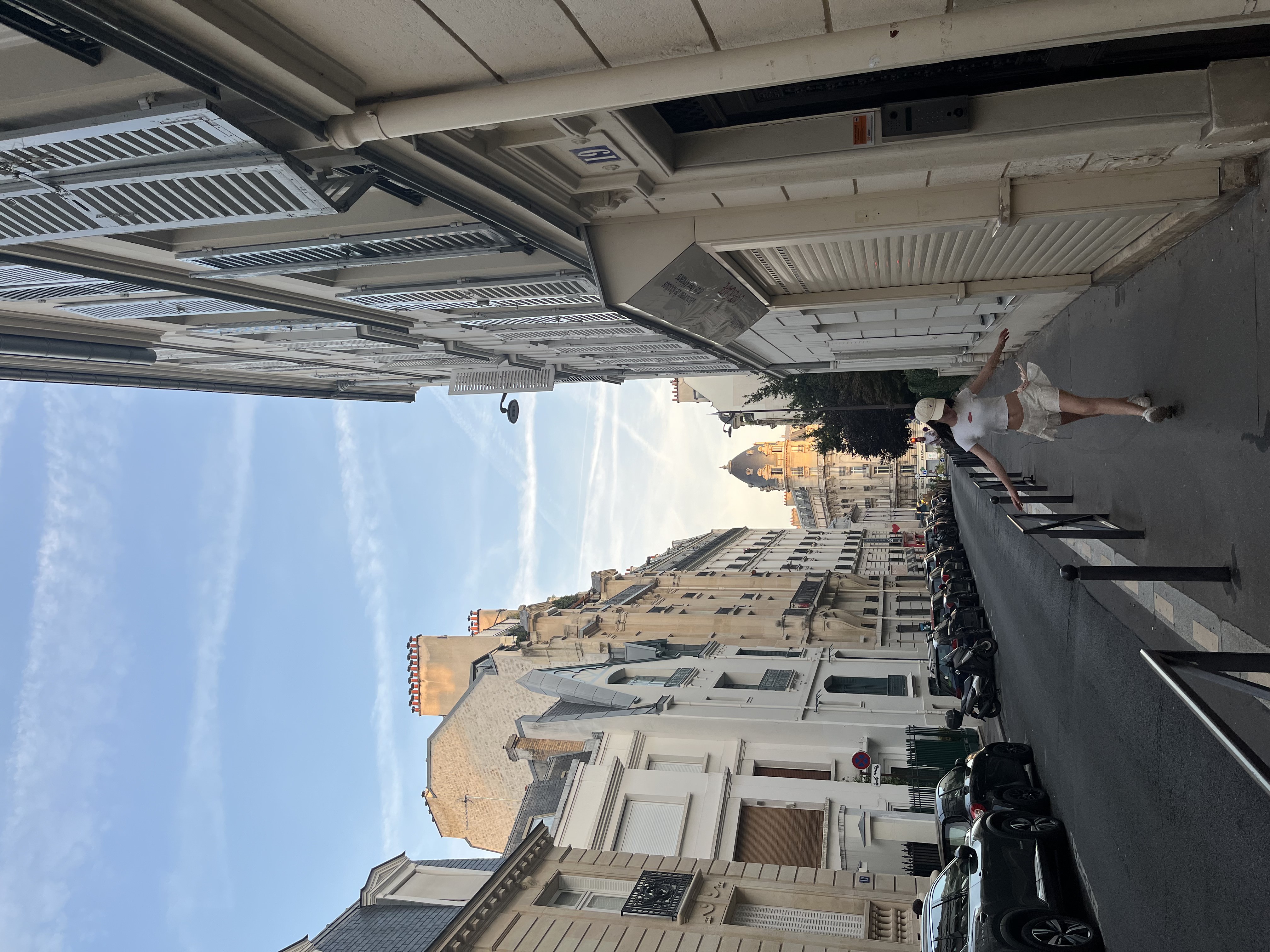 a picture of me in a white shirt with a beige skirt and beige cap on, skipping towards the camera on a street in paris.