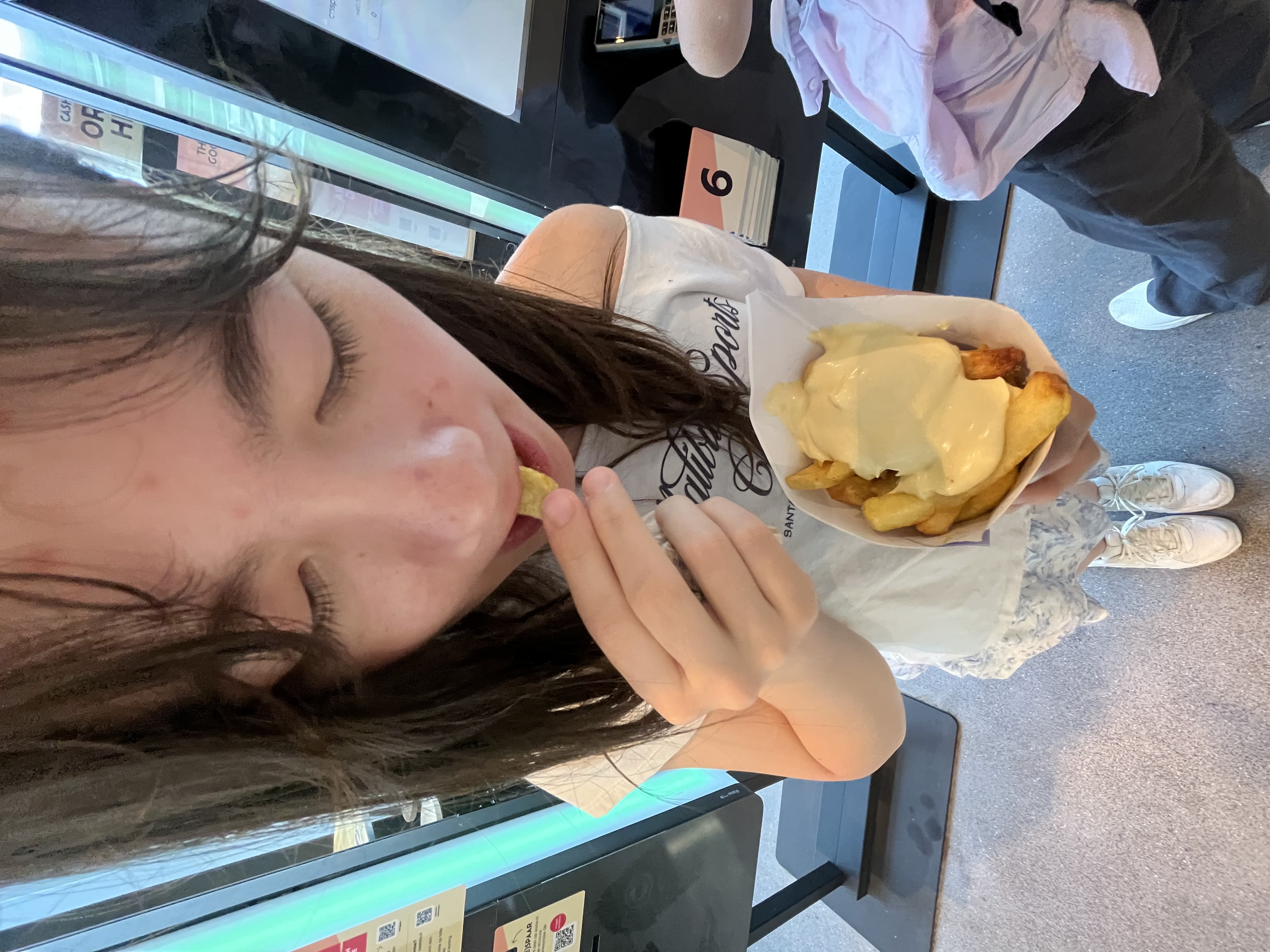 A 0.5x picture of me eating fries with a glop of mayo on it in a blue cone in amsterdam.