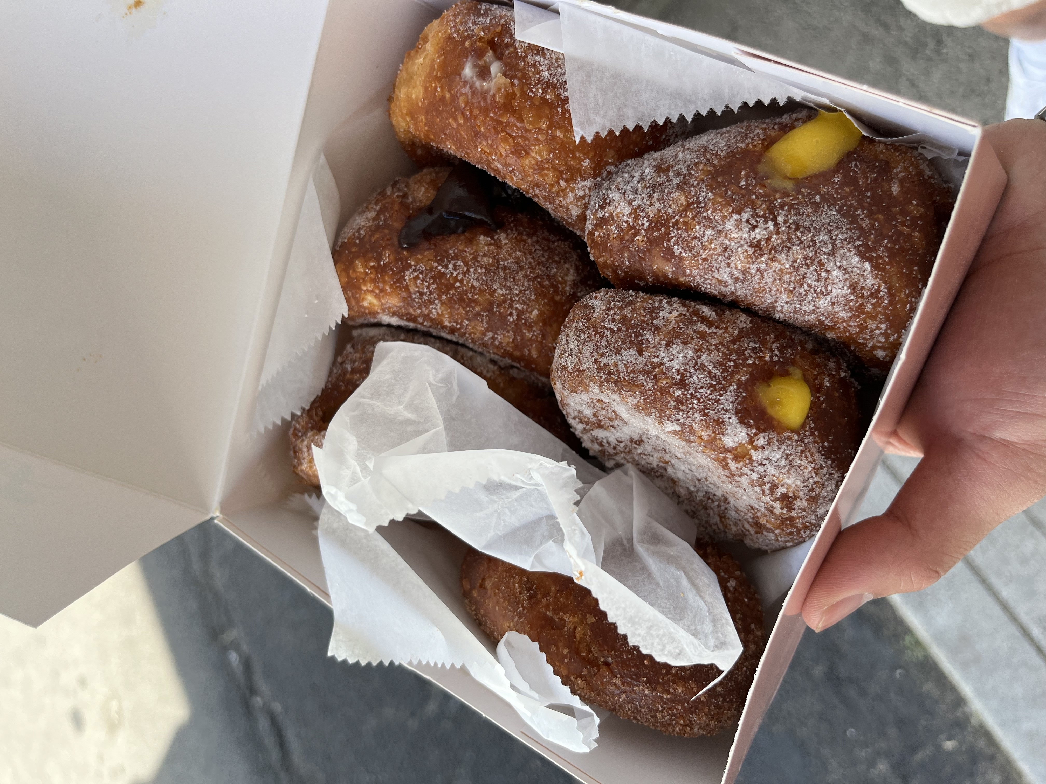 A picture of a box of six malassadas with powdered sugar on them from hawaii.